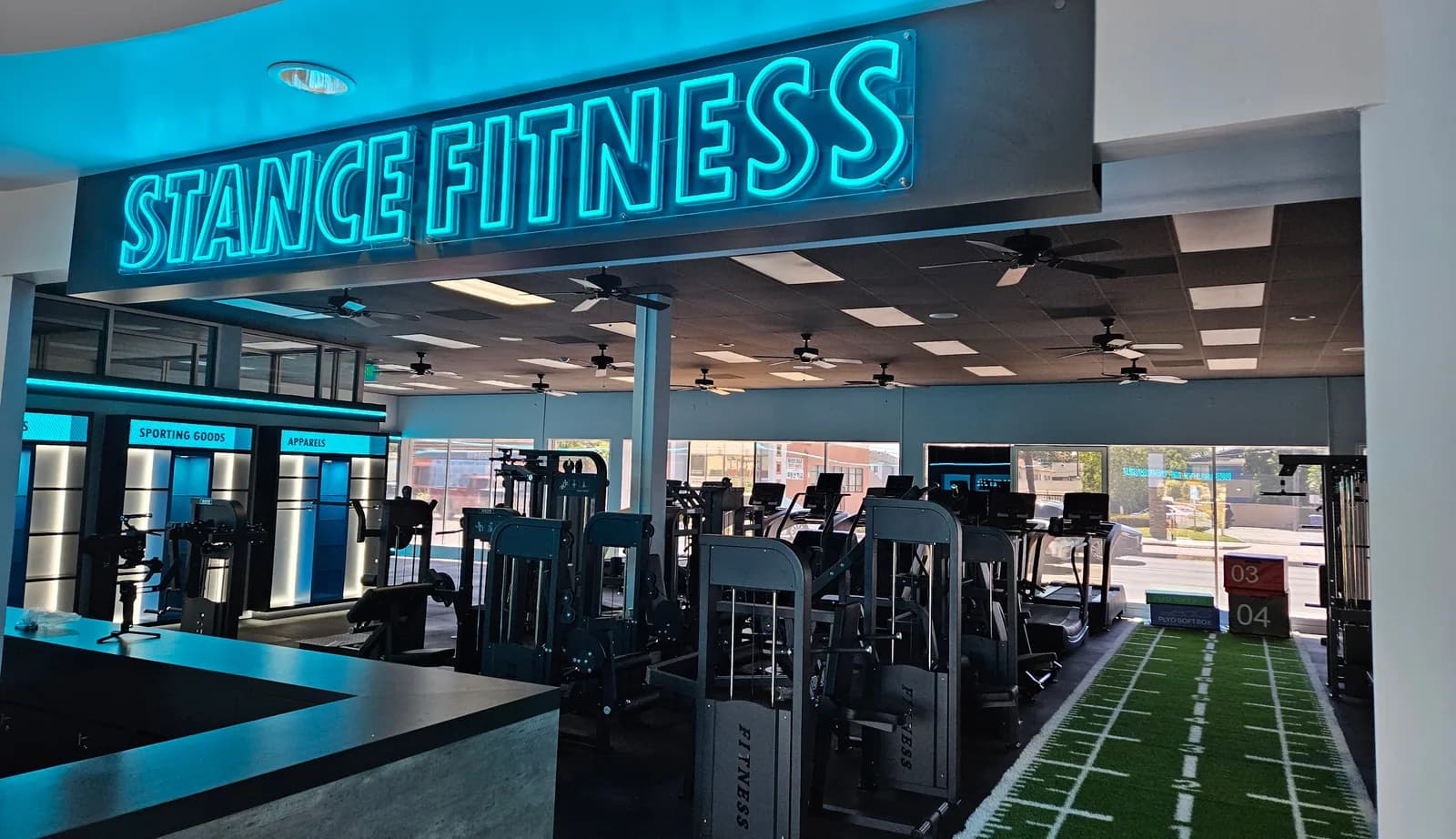 Stance Fitness gym interior with neon sign, exercise machines, and turf training area