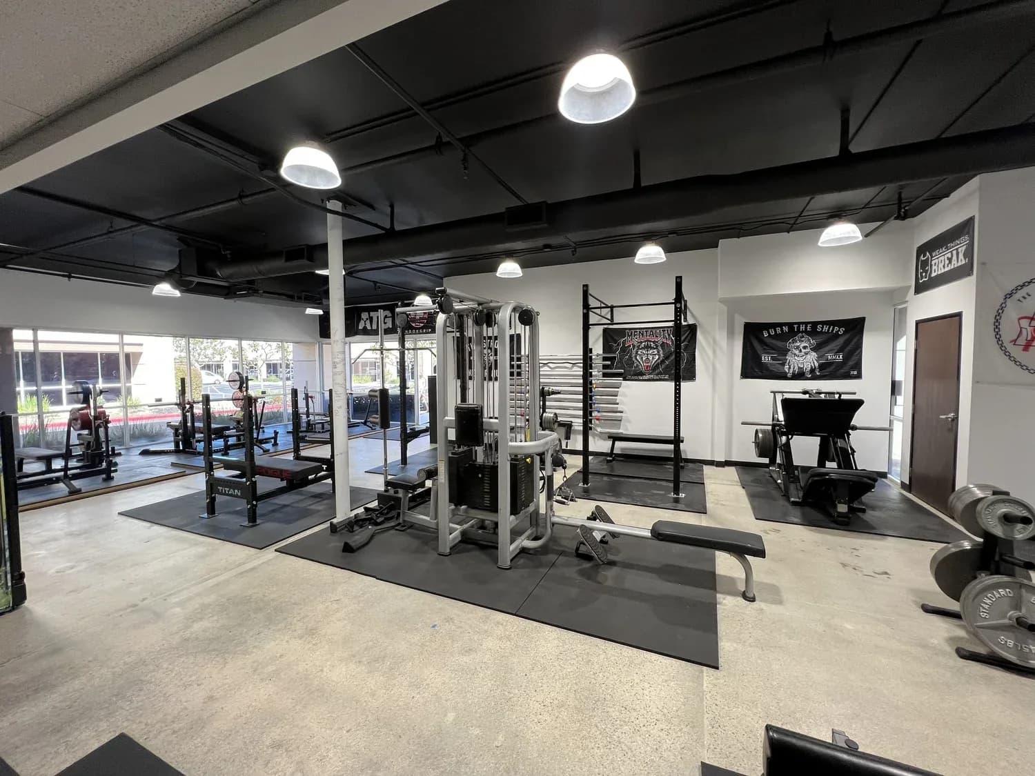 Gym interior with multiple weight machines, racks, and free weights on dark mats