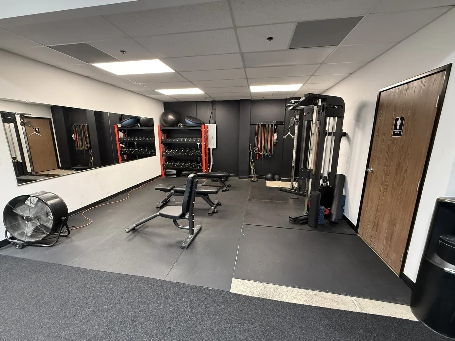 Bright gym interior with dumbbells, weight racks, strength machines, and mirrored walls