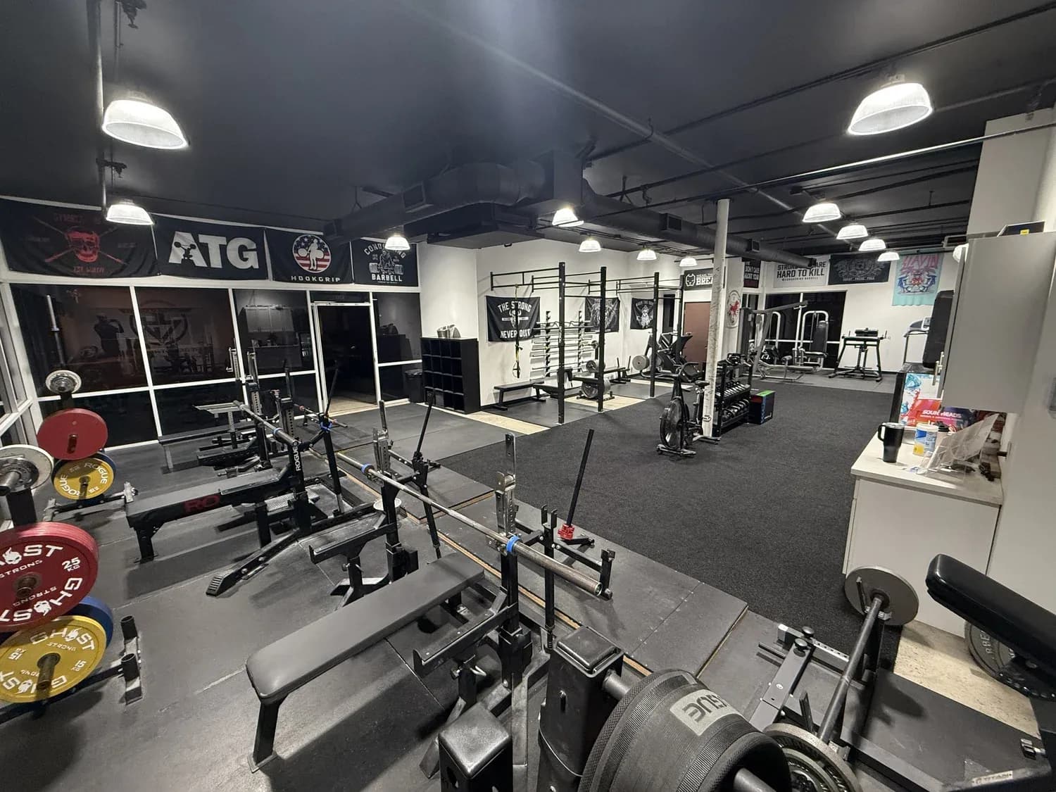 Spacious gym interior with barbells, benches, and exercise equipment under bright overhead lights