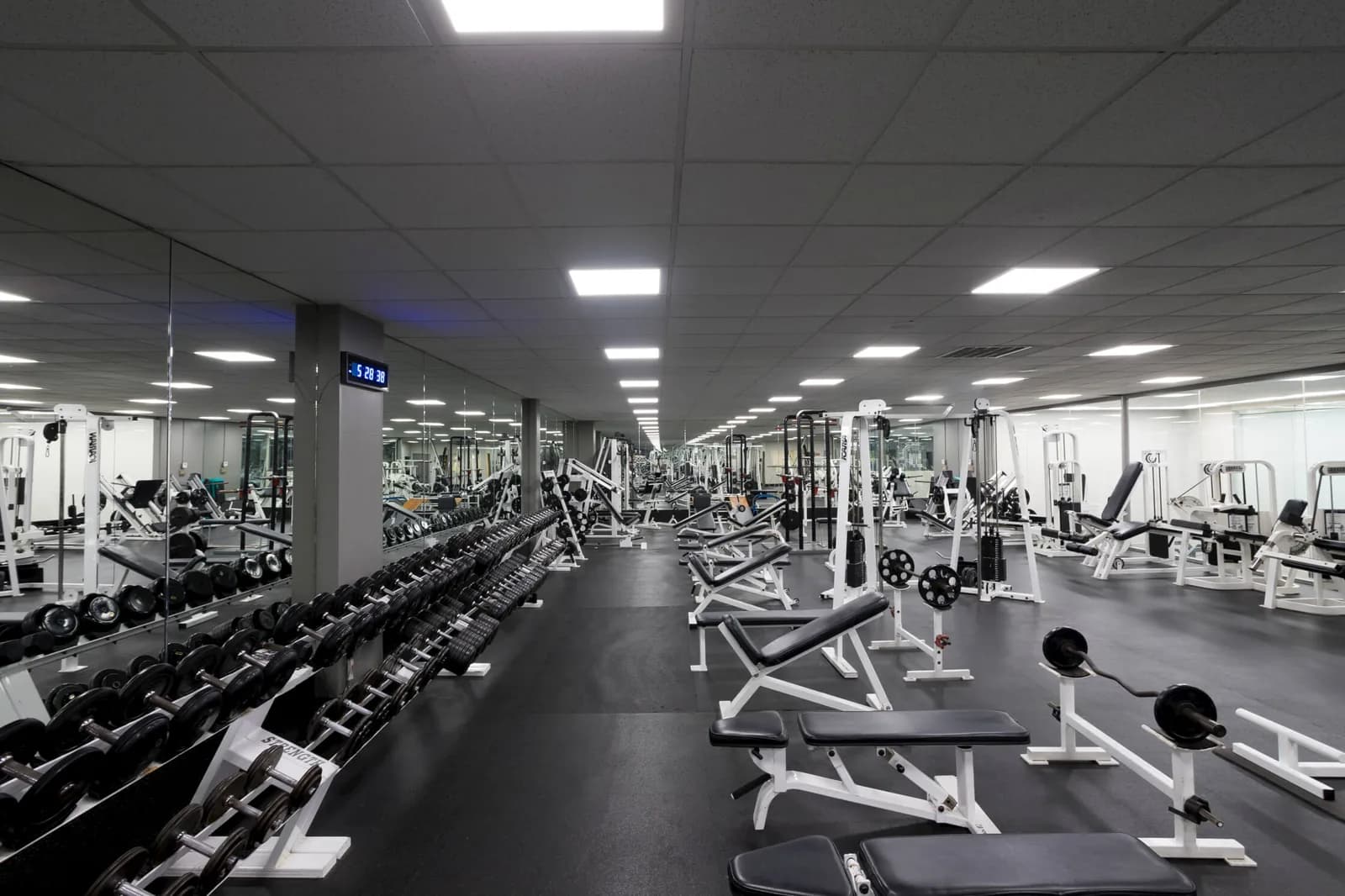 Modern gym with extensive weight equipment, dumbbells, and training machines under bright ceiling lights