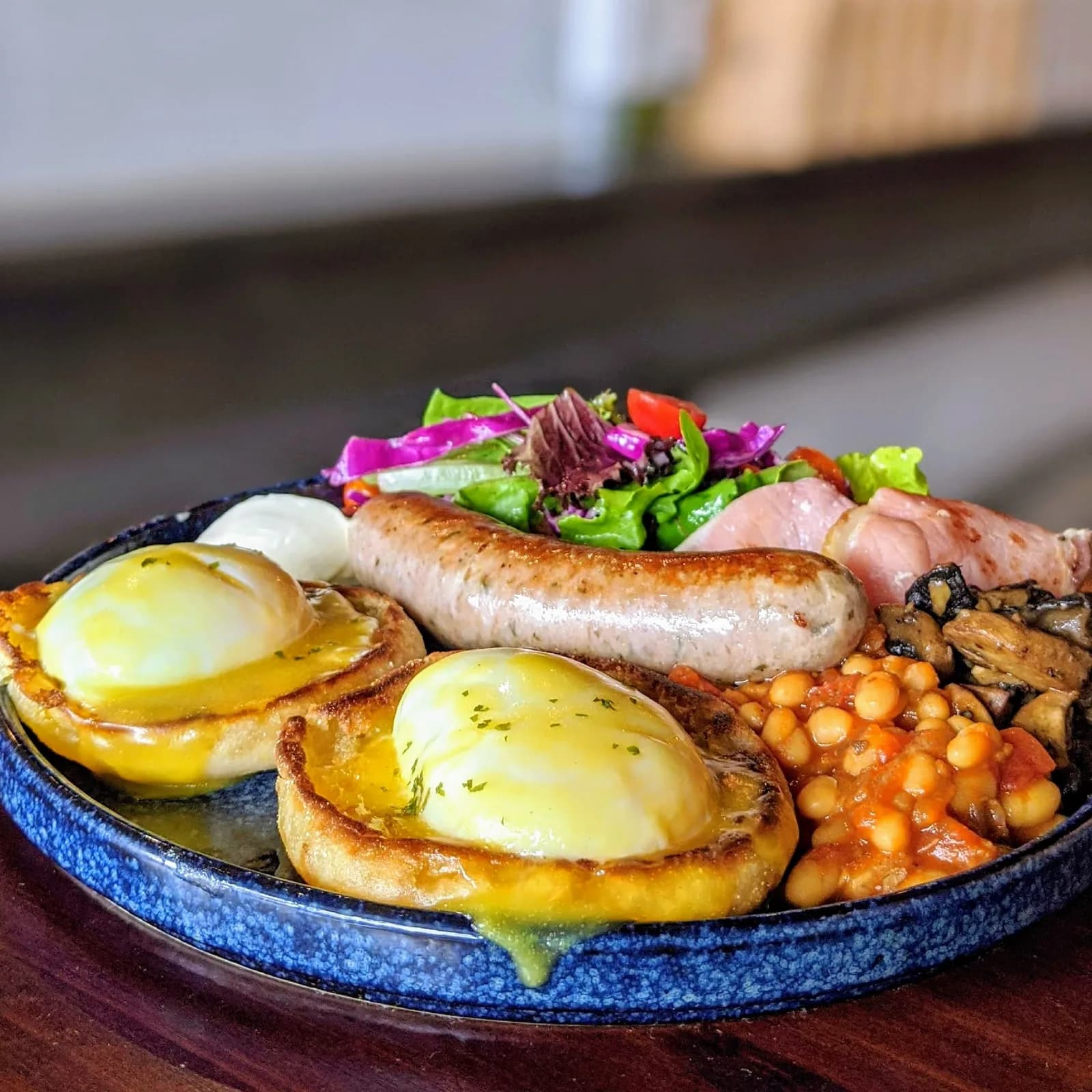 Brunch plate with poached eggs on toast, sausage, chickpeas, and fresh salad on cast iron plate