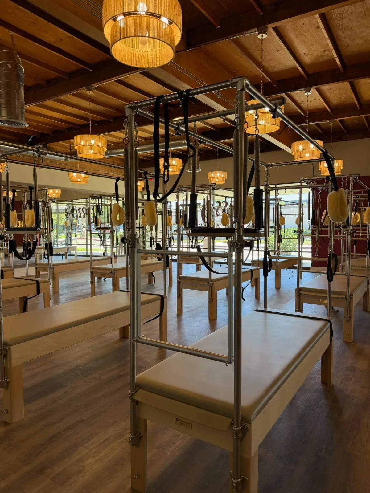 Pilates studio with several black-framed reformer machines and wooden benches under a wooden ceiling