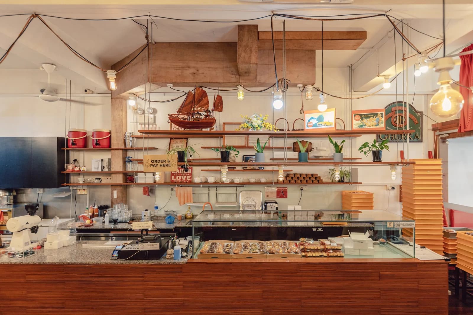 Patisserie counter with pastries, shelving with plants and decor, wooden beams and hanging pendant lights