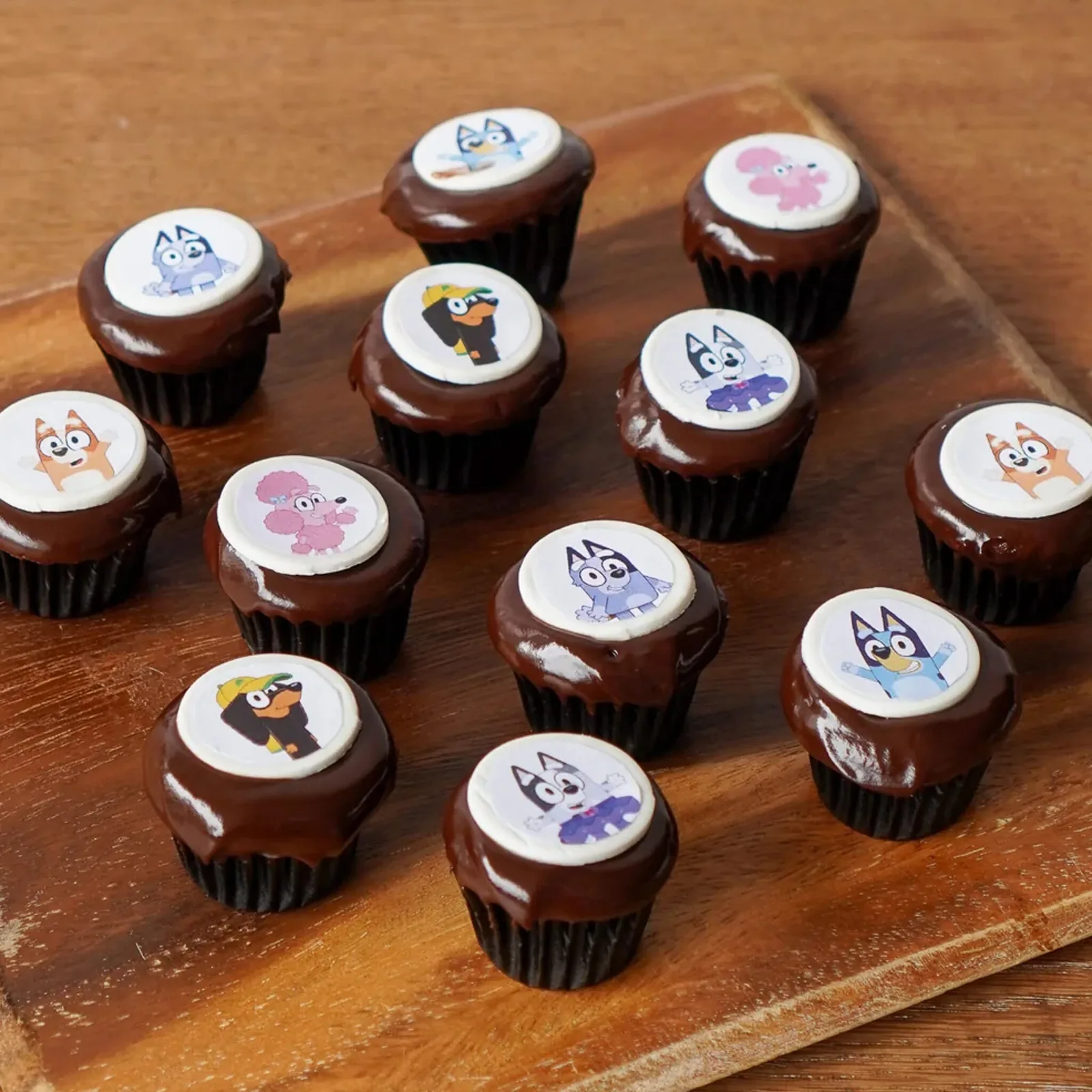 Chocolate cupcakes with cartoon character toppers on a wooden serving board