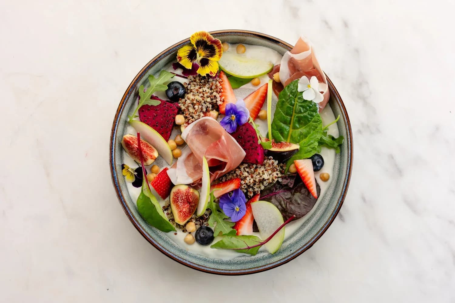 Gourmet salad bowl with greens, quinoa, figs, berries, prosciutto and colorful edible flowers