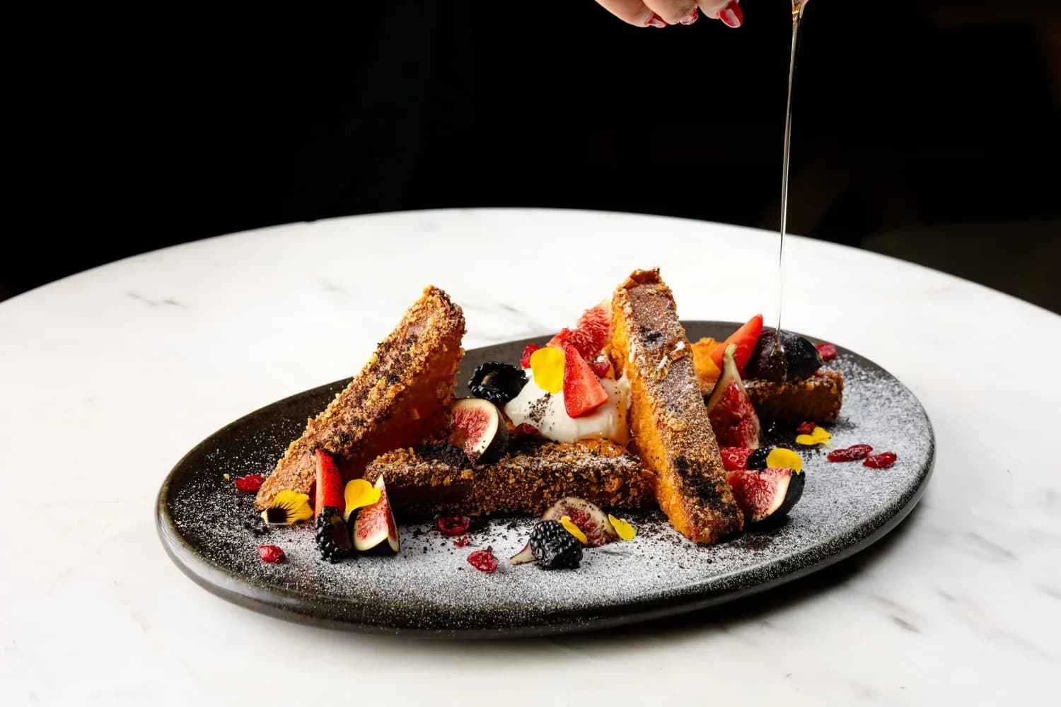 Gourmet dessert plate with toasted bread, berries, and fruit garnish with sauce being drizzled on top.