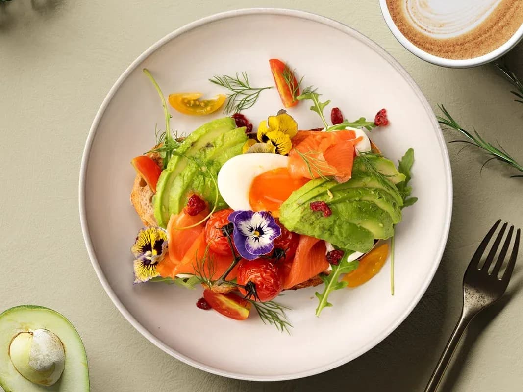 Gourmet avocado toast with salmon, egg, and edible flower garnish on white plate
