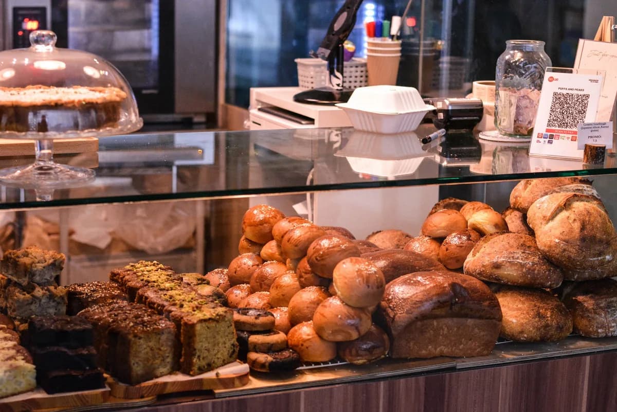 Bakery display case with fresh breads, pastries, and cakes under glass, service counter in background