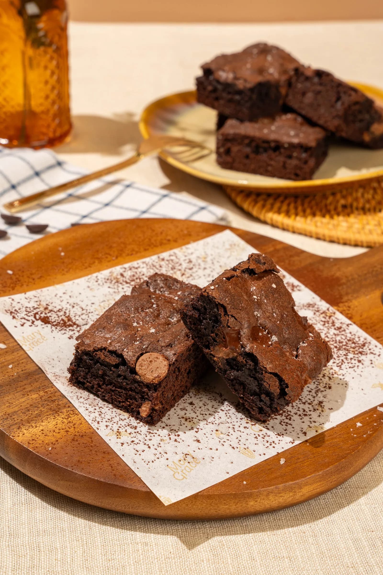 Chocolate brownies dusted with cocoa powder on a wooden plate with a beverage and more brownies in the background