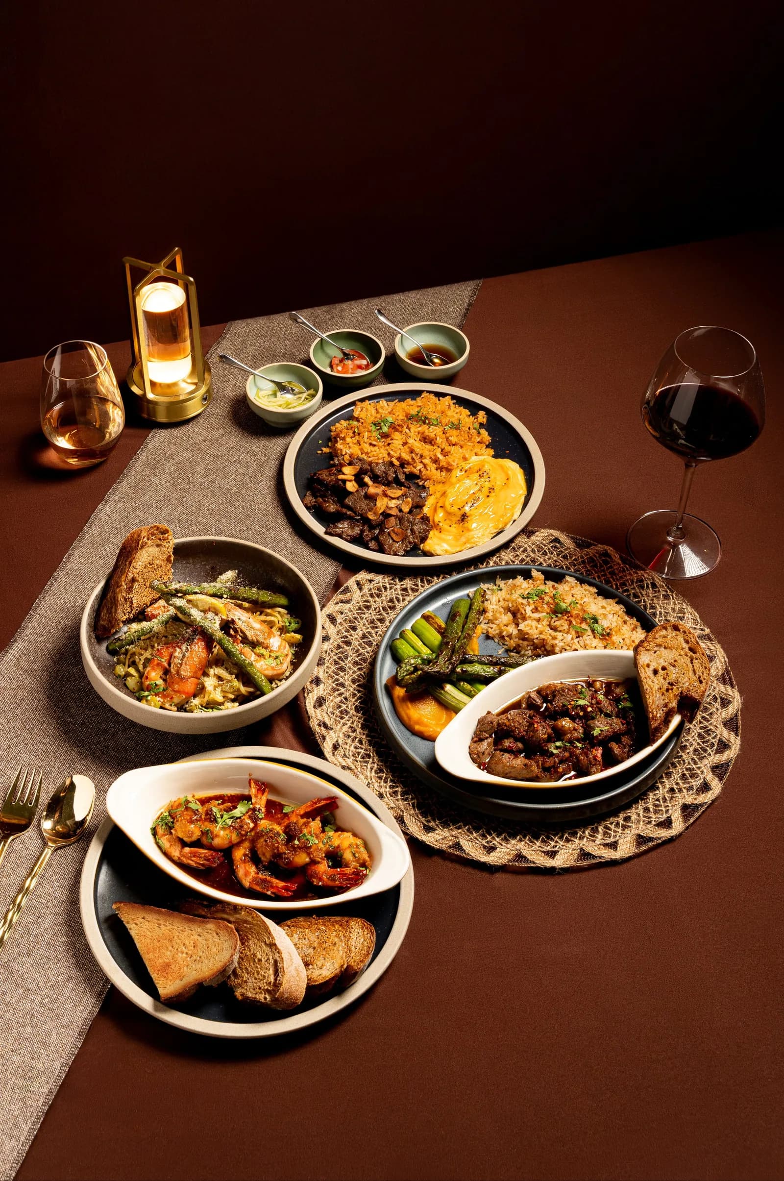Restaurant table with multiple plated dishes, wines, and condiments in warm lighting