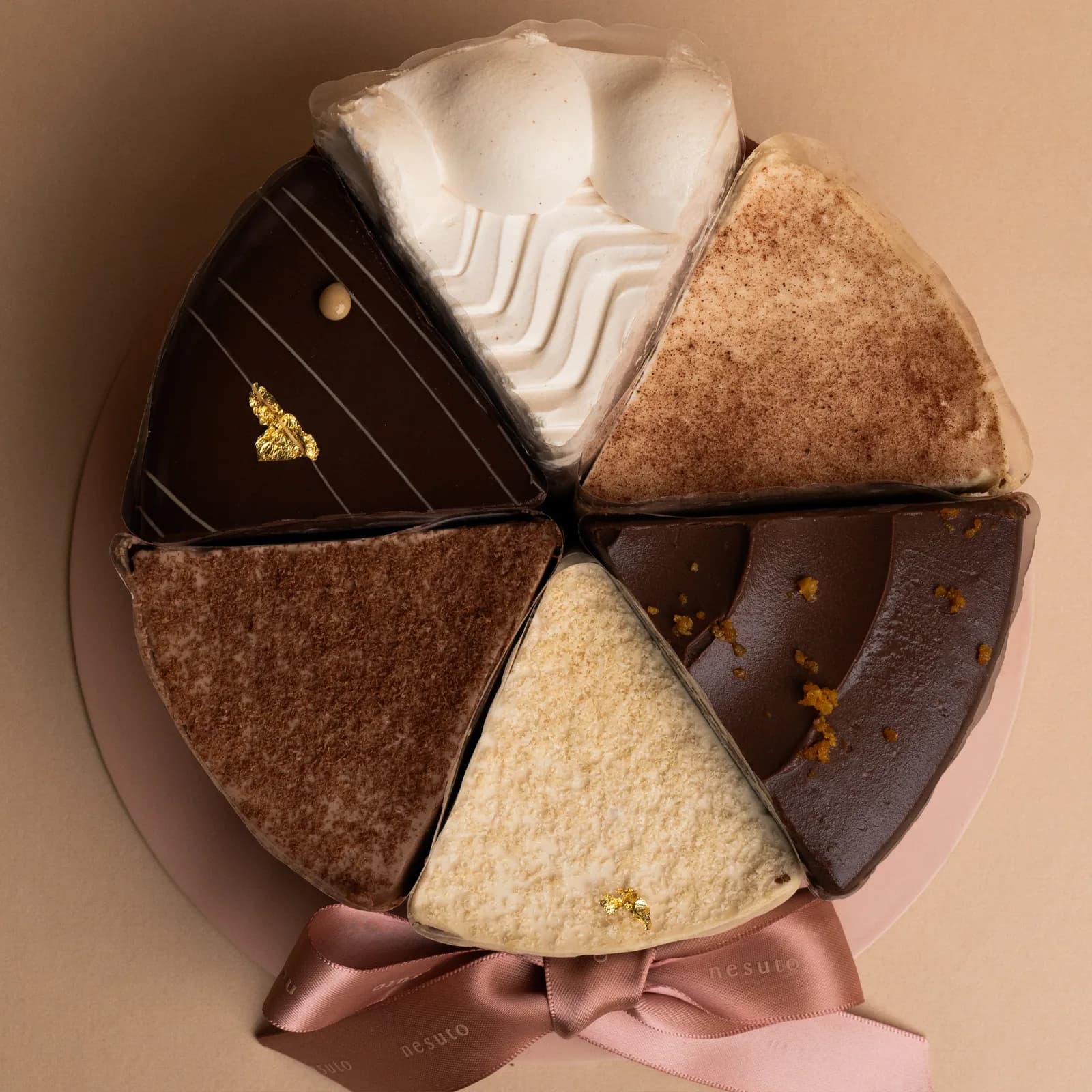 Six triangular chocolate cake slices arranged in a circle with whipped cream, cocoa powder, and gold leaf decorations.
