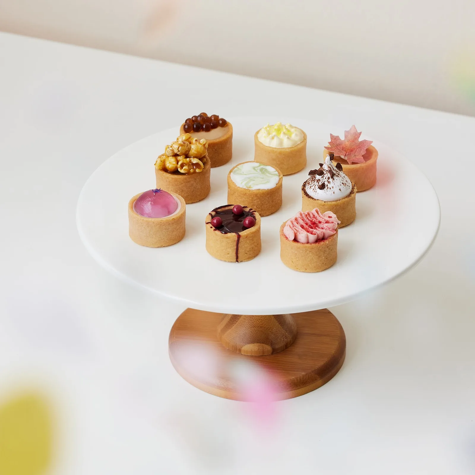 Nine gourmet tarts with diverse toppings displayed on a white pedestal plate.
