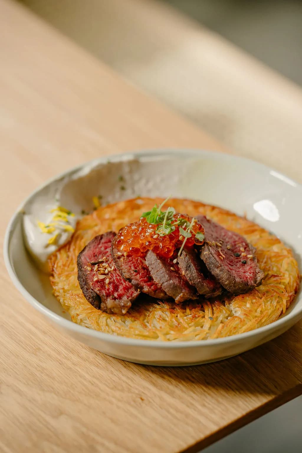Sliced rare beef with caviar and herbs on rosti, in a white bowl