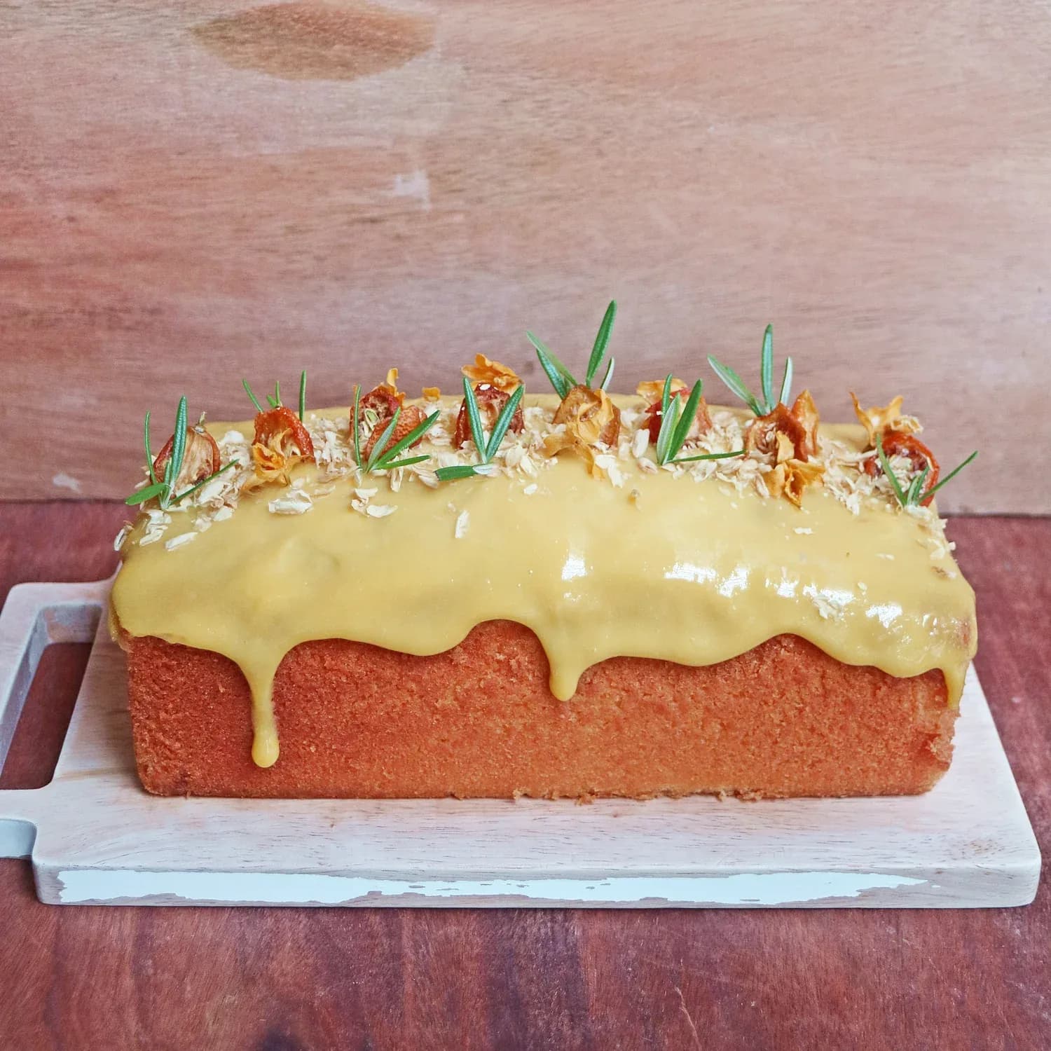Carrot cake loaf with yellow glaze, coconut, candied orange, and rosemary garnish
