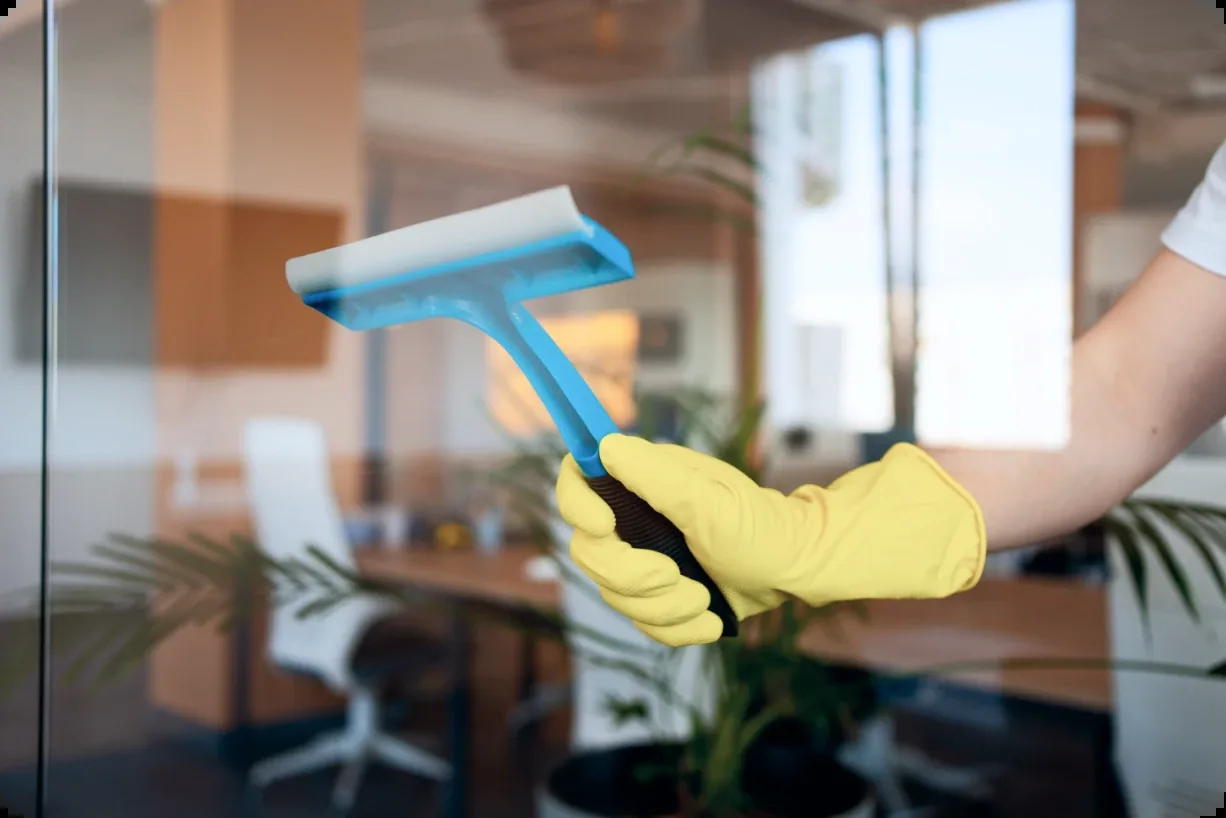 Worker cleaning glass with blue squeegee and yellow gloves in office space