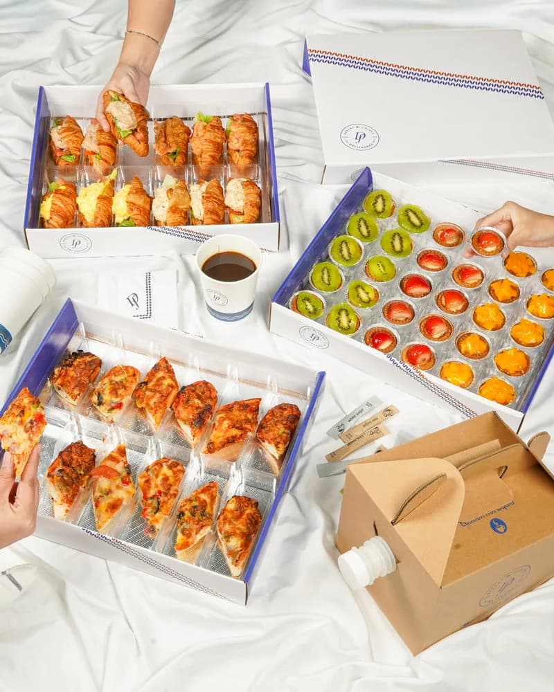 Branded boxes displaying croissants, fruit tarts, and other pastries with a coffee cup on white background