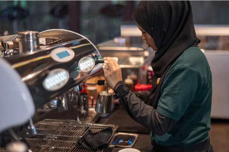 Barista steaming milk using an espresso machine wand