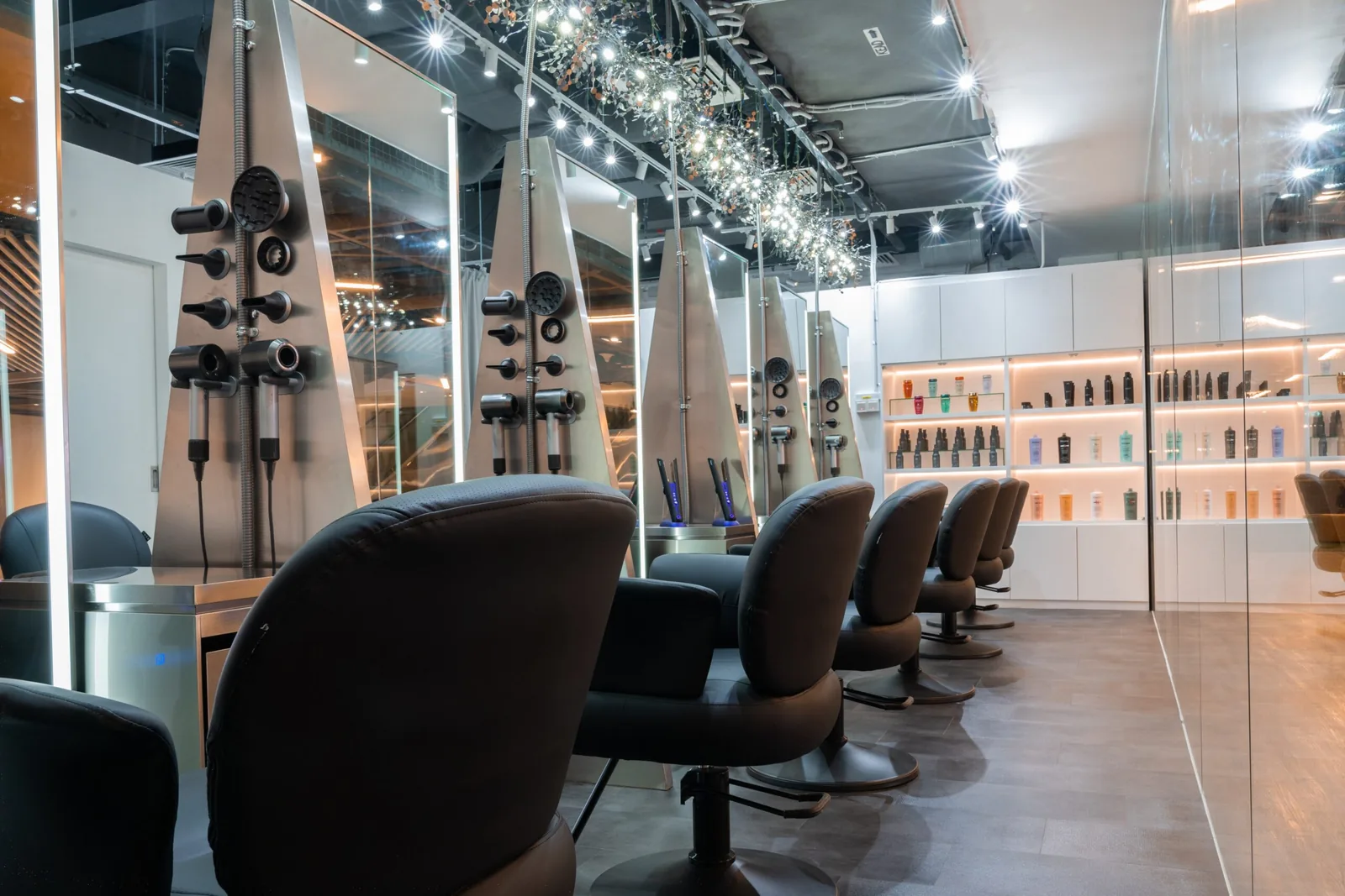 Modern hair salon with black styling chairs, illuminated mirrors, and product shelves