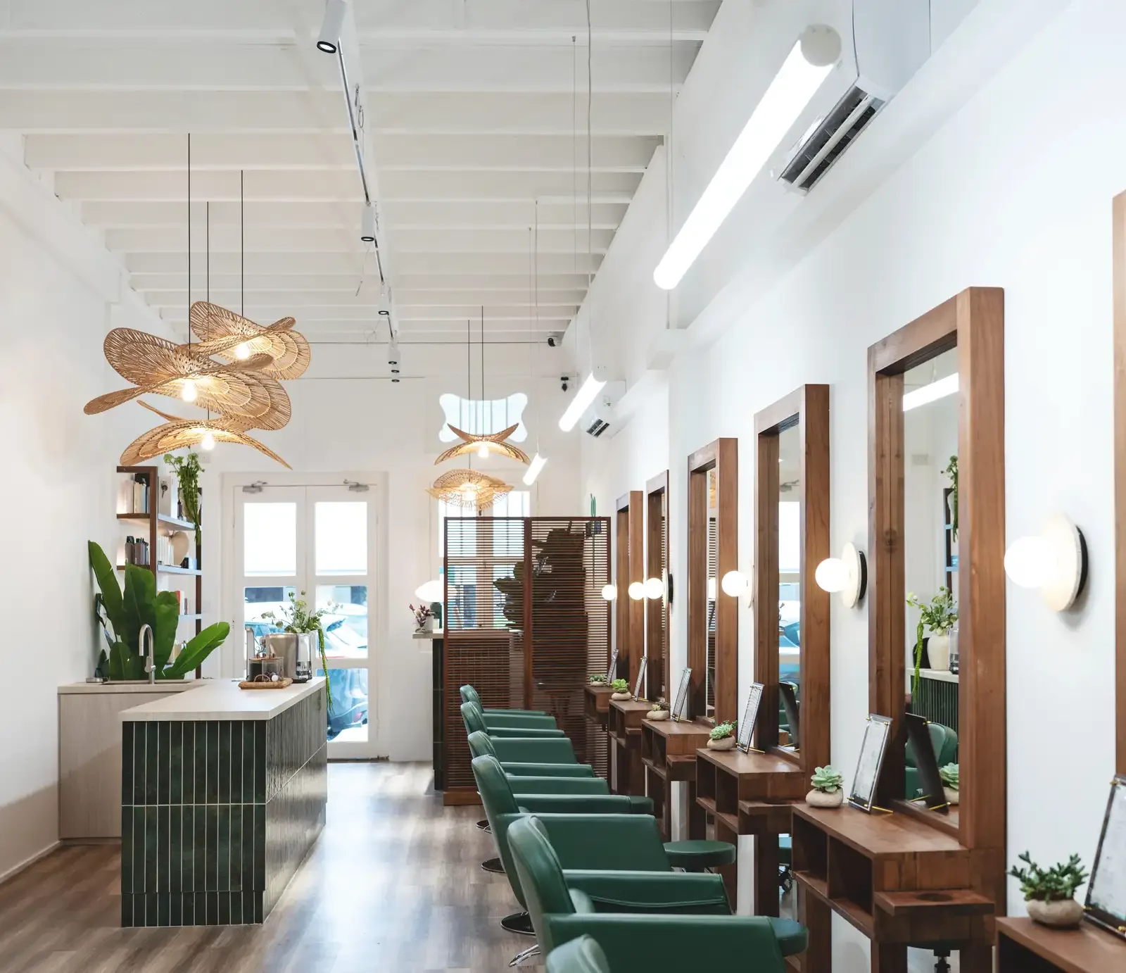 Hair salon interior with green styling chairs, wooden mirrors, and woven pendant lights