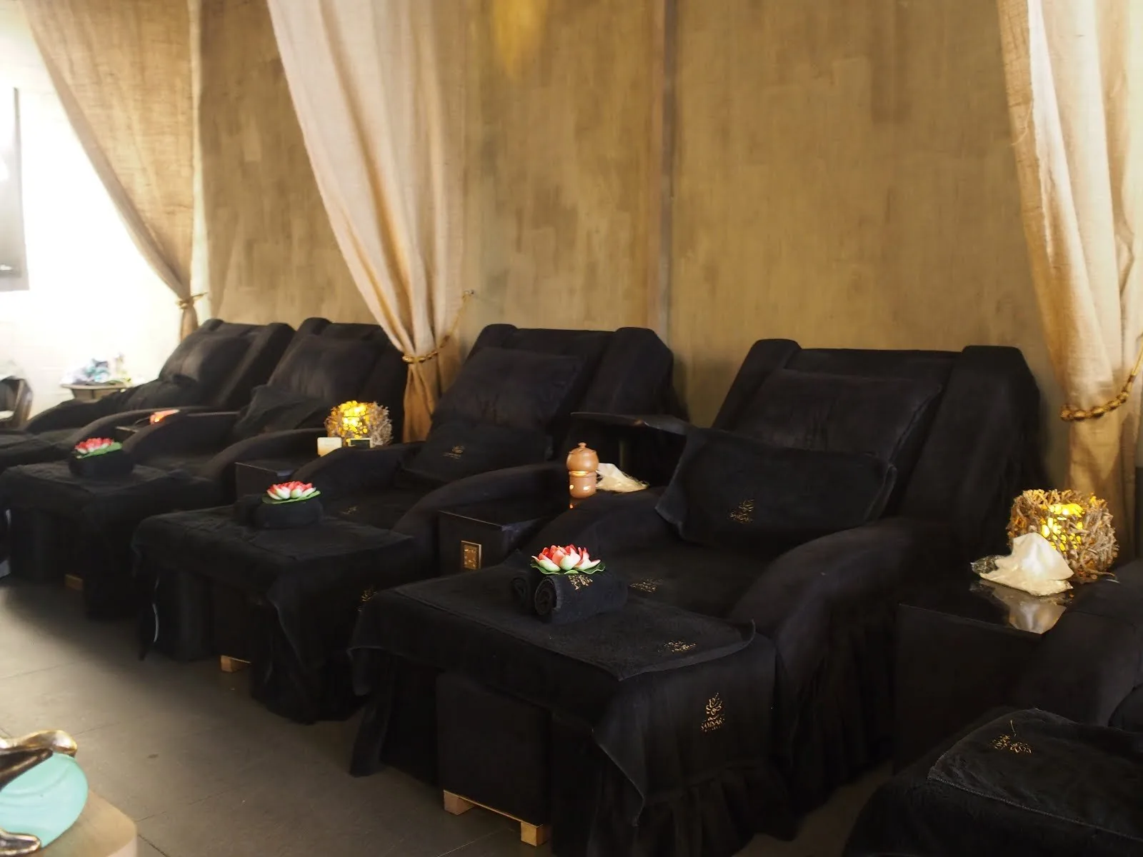 Spa relaxation room with black massage chairs, gold curtains, and lotus flower decorations