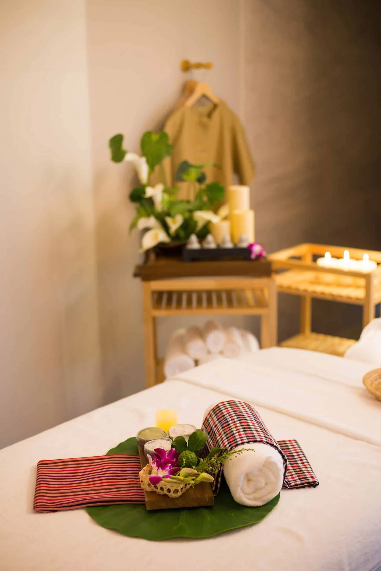 Spa room with decorated bed, fresh flowers, rolled towels, and wellness amenities on wooden furniture.