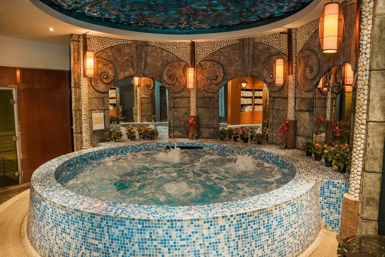 Circular hot tub with blue tile in an ornate spa room with mirrors and hanging lights
