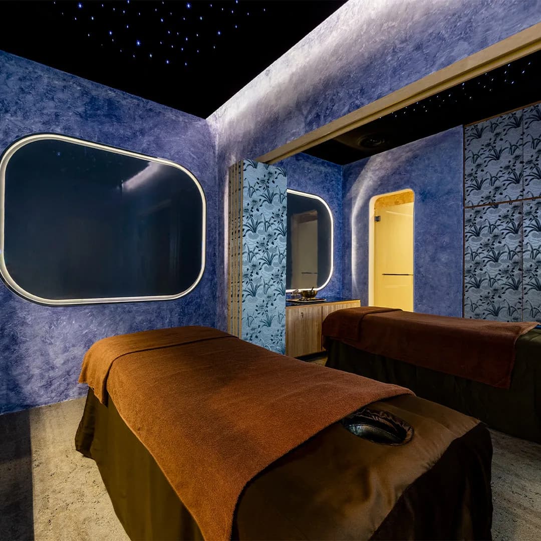 Spa treatment room with blue walls, lit mirrors, massage beds, and starlit ceiling design