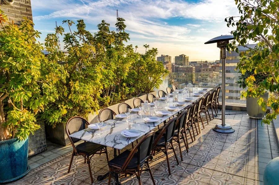 Elegant rooftop terrace with marble dining table, black chairs, green plants, and city skyline view