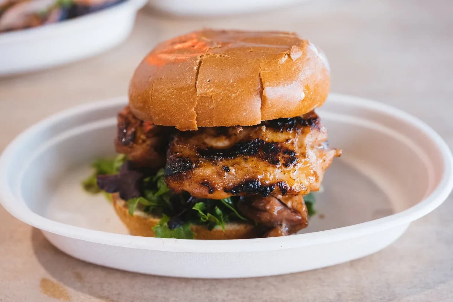 Gourmet chicken burger with bacon and greens on toasted bun, white plate