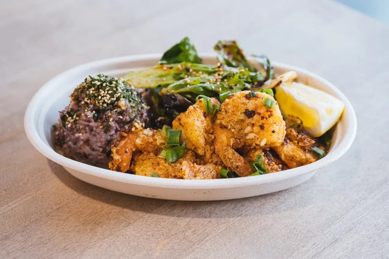 Fried shrimp with roasted vegetables and purple potato in a white bowl, garnished with sesame seeds and green onions.
