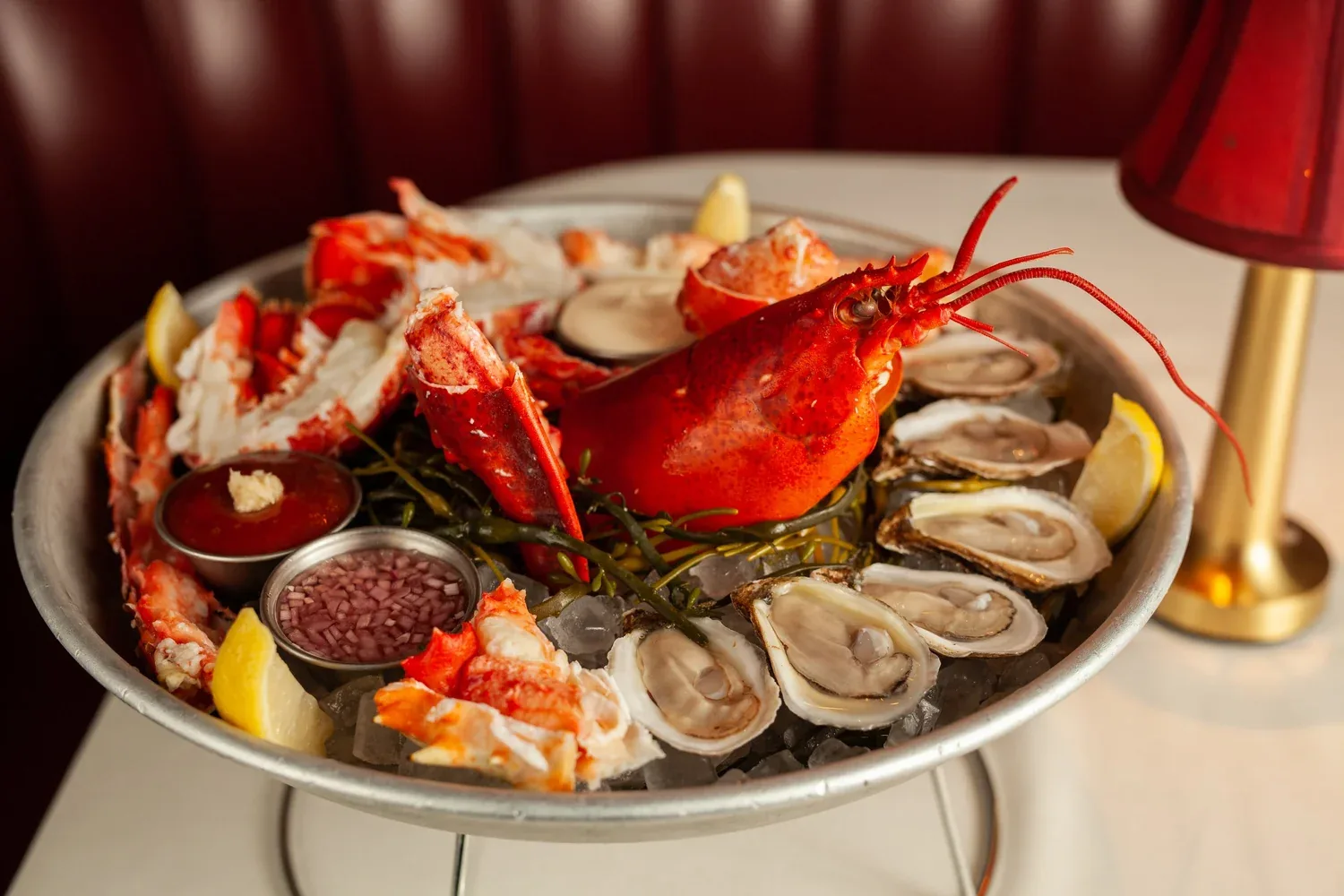 Seafood platter with whole lobster, oysters, and lobster tail on ice with lemon and sauce