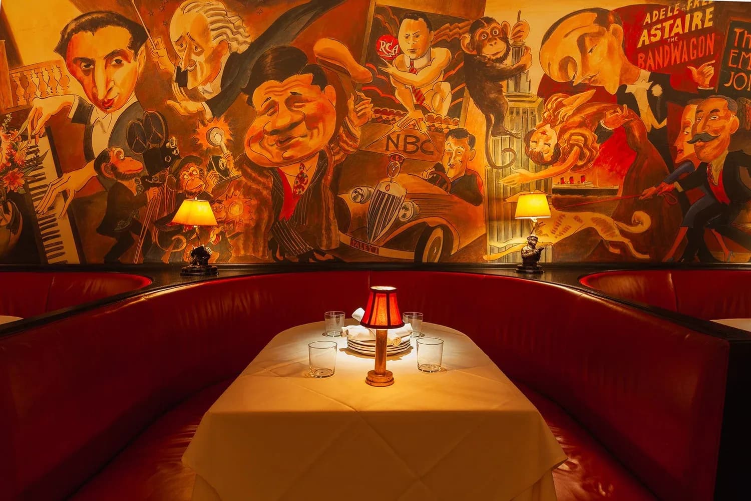 Vintage-styled restaurant booth with red leather seating, white tablecloth, and elaborate entertainment murals on walls