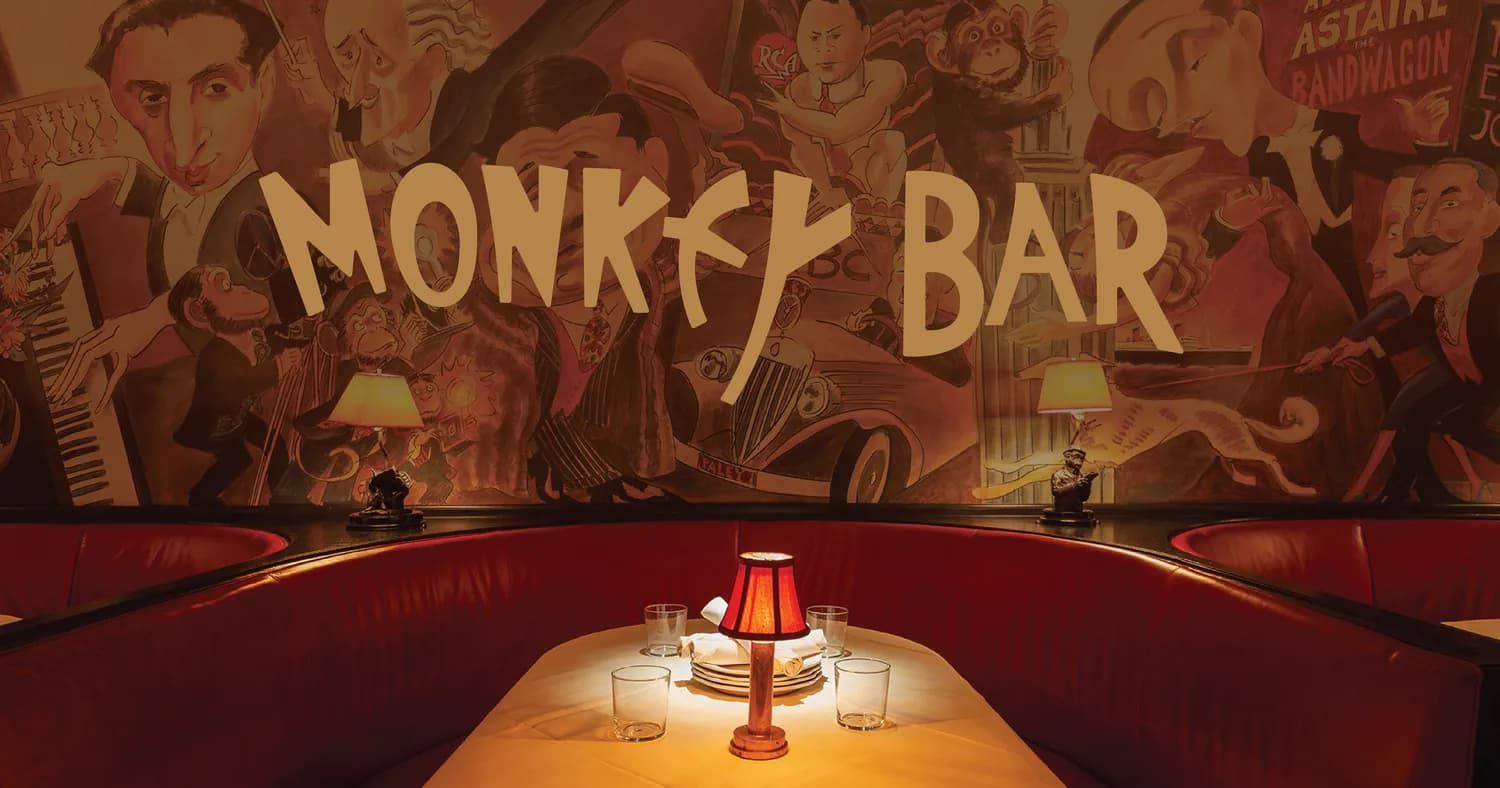 Monkey Bar interior with red booth seating, table lamp, and art deco wall mural