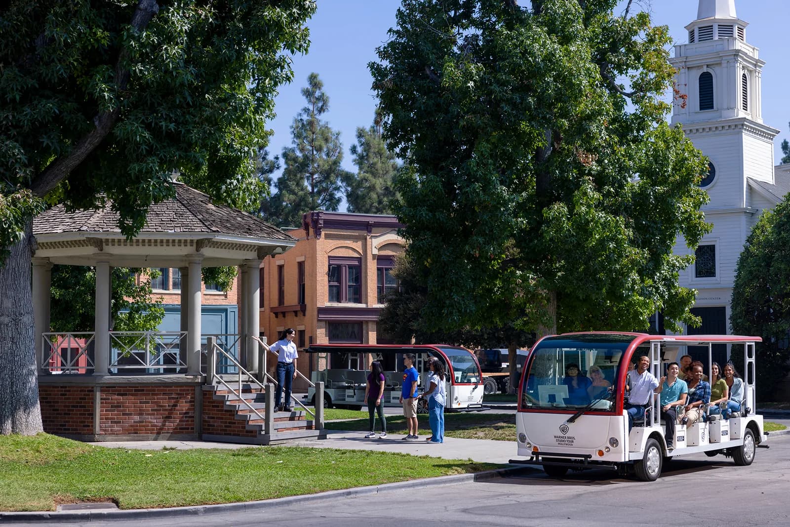 Red and white trolley with passengers touring Warner Bros. Studio backlot with historic buildings