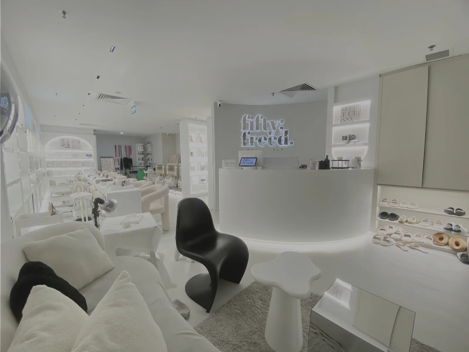Modern nail salon interior with white curved reception desk, black chairs, and product displays