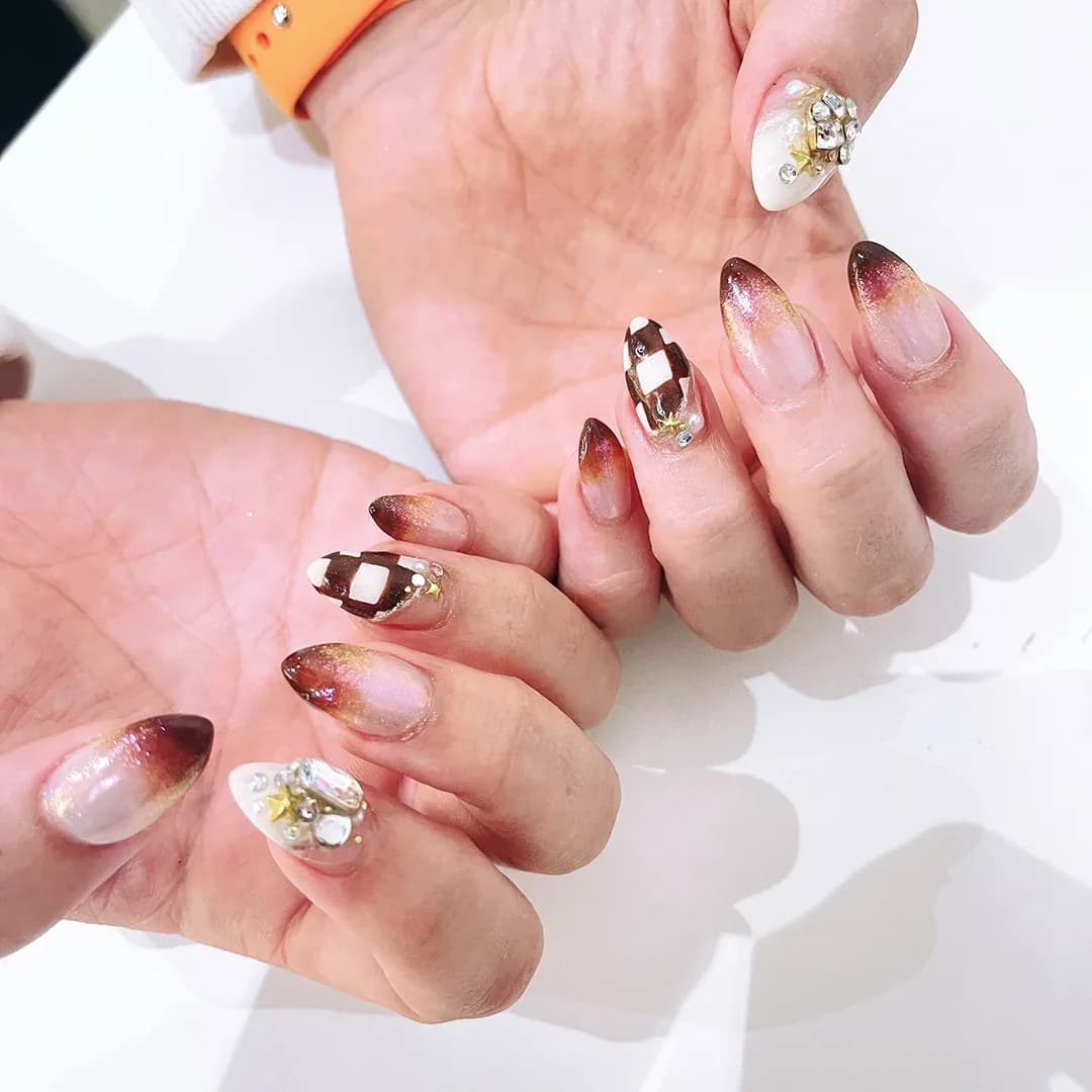 Manicured nails with burgundy ombre, gold details, and rhinestone designs