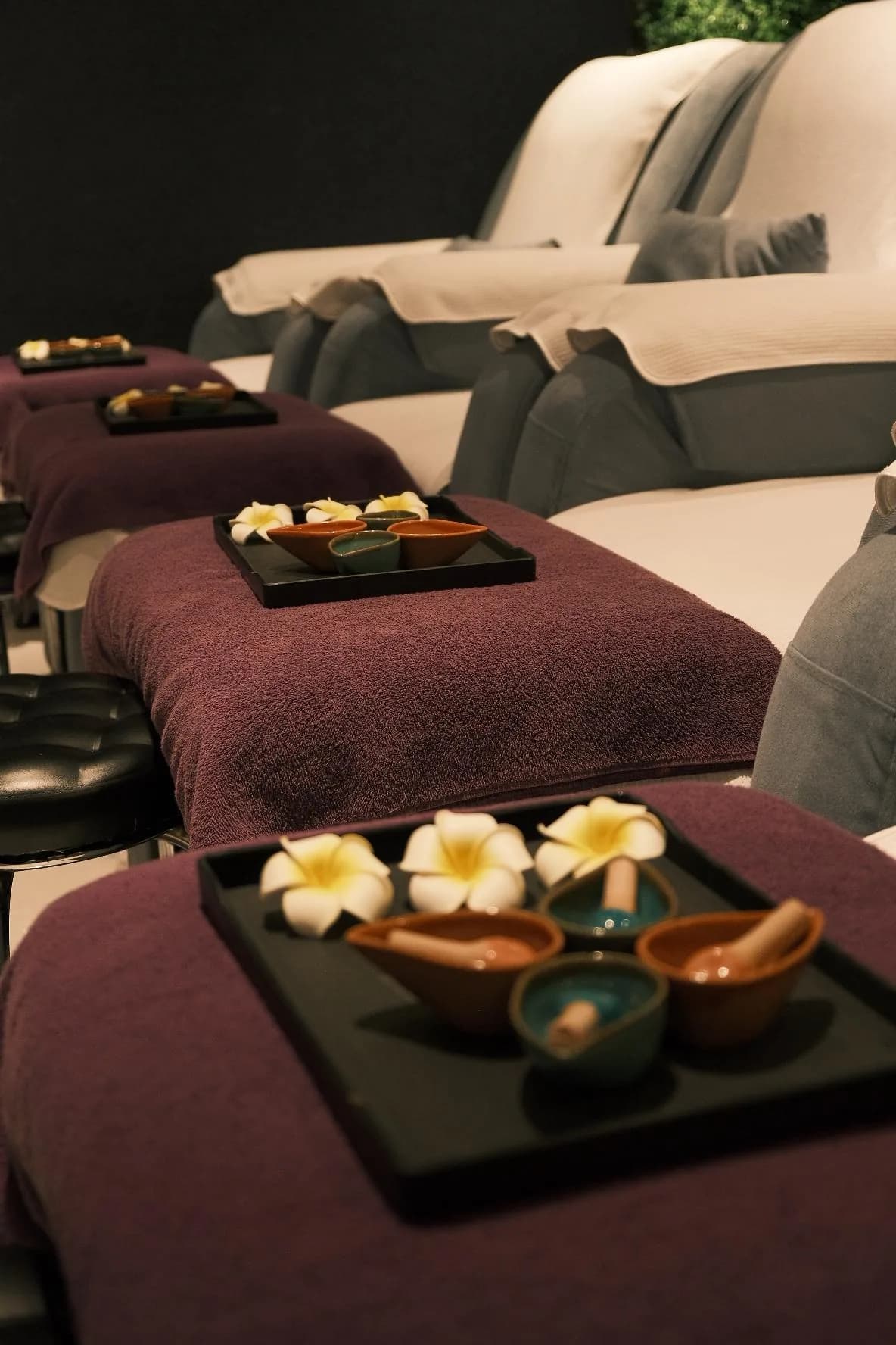 Spa relaxation lounge with cream-colored recliners, burgundy linens, and floral spa treatments on dark tables.