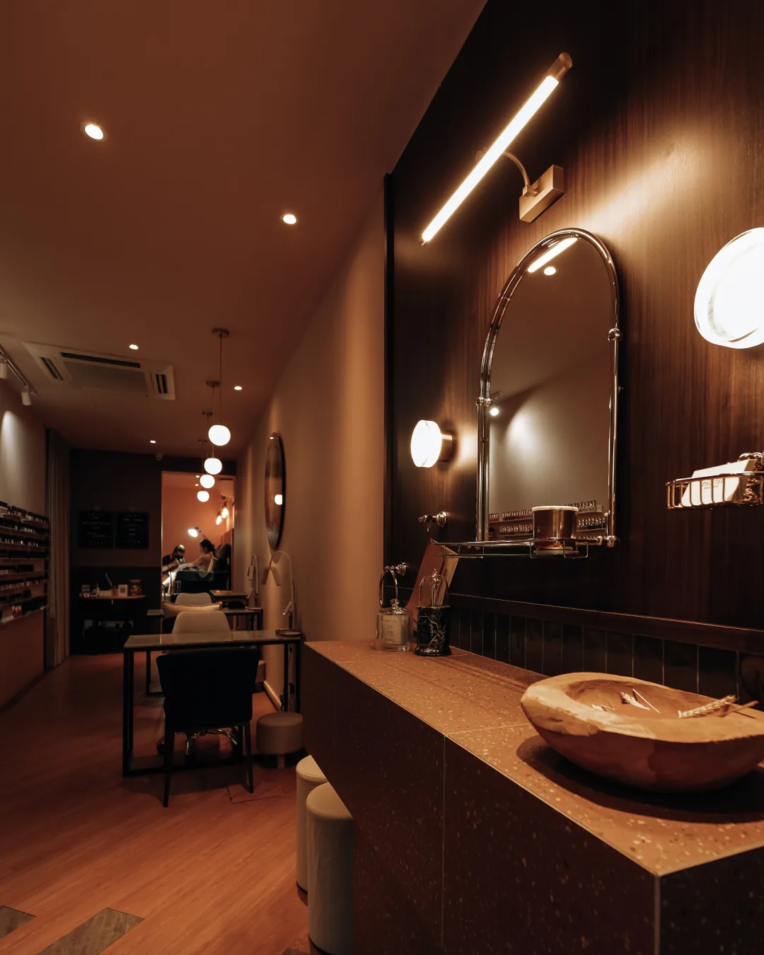 Modern nail salon interior with illuminated mirror, wooden counter, and warm lighting throughout the space
