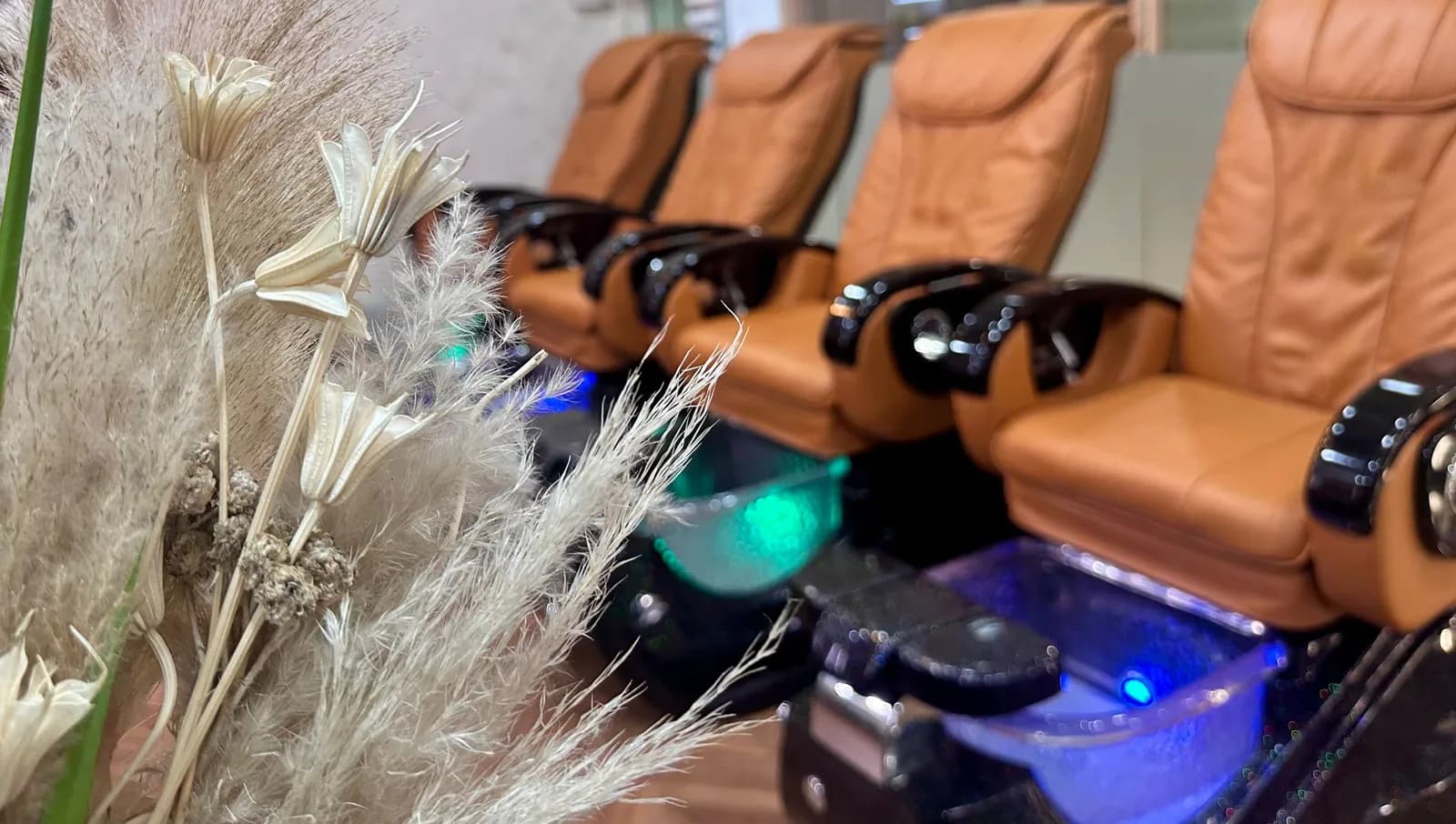 Pedicure chairs with warm lighting and pampas grass decoration in nail salon