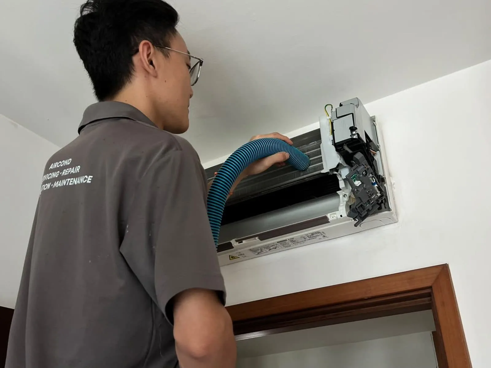 Technician servicing indoor air conditioning unit with blue hose