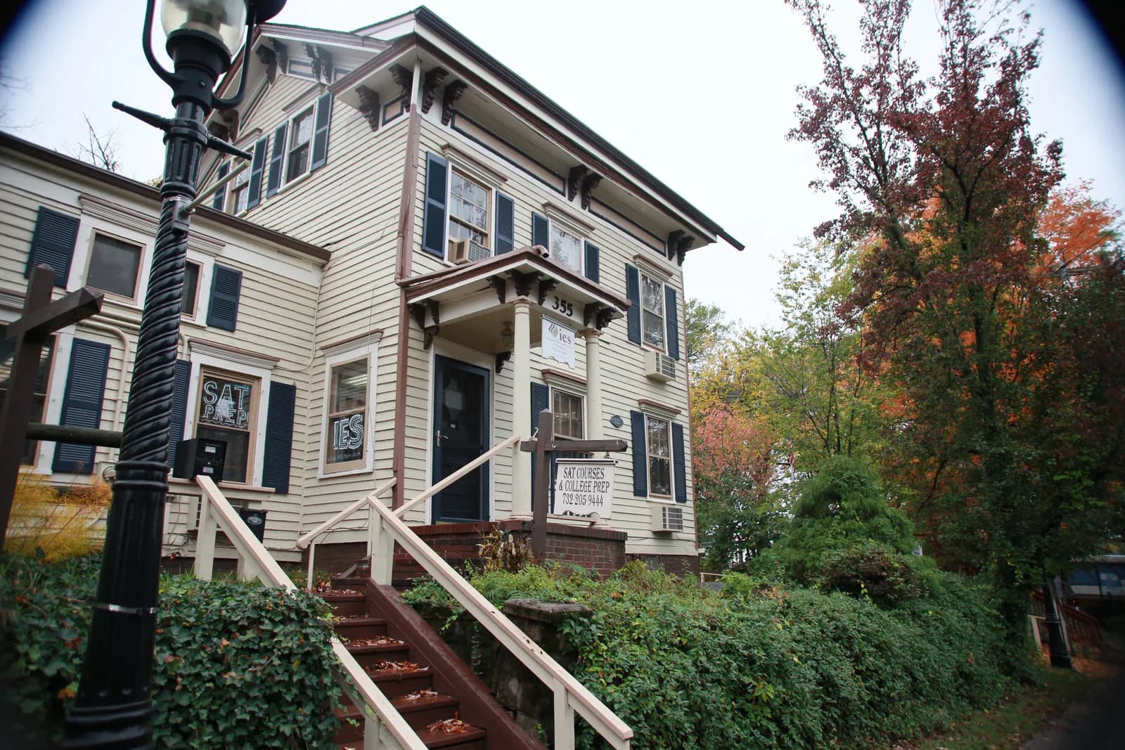 Victorian building housing IES Test Prep with cream siding, dark shutters, and front entrance stairs surrounded by fall foliage