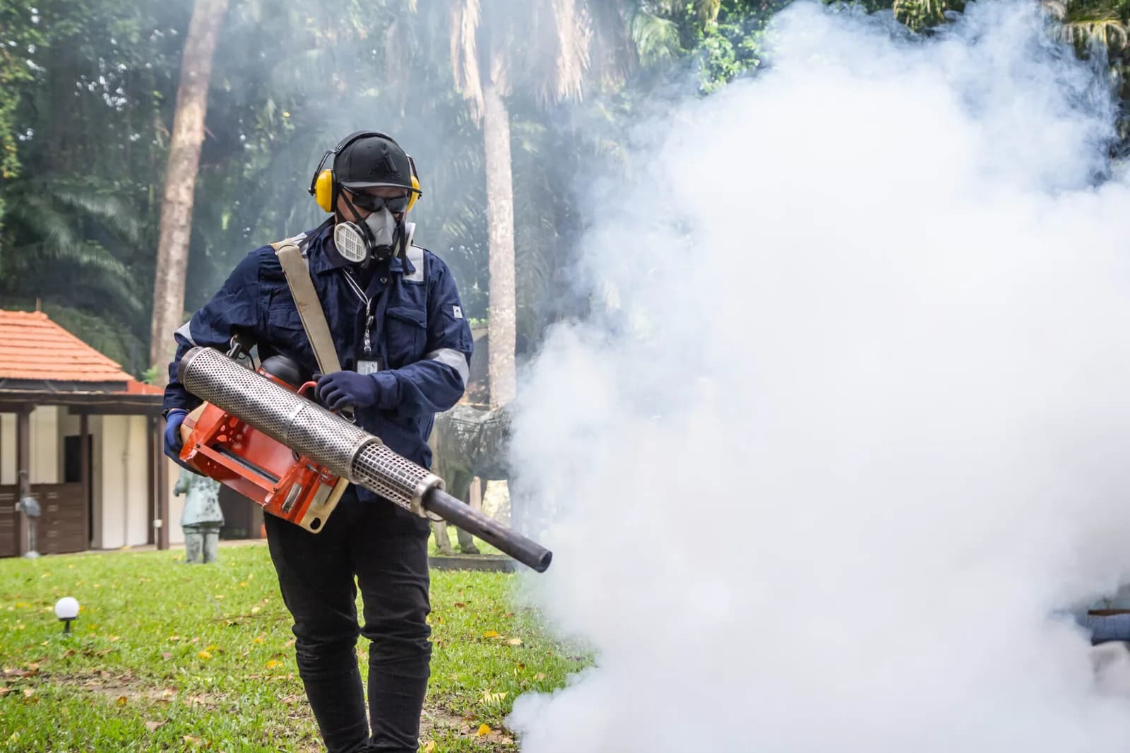 Pest control worker in protective gear using a fogging machine to spray treatment outdoors