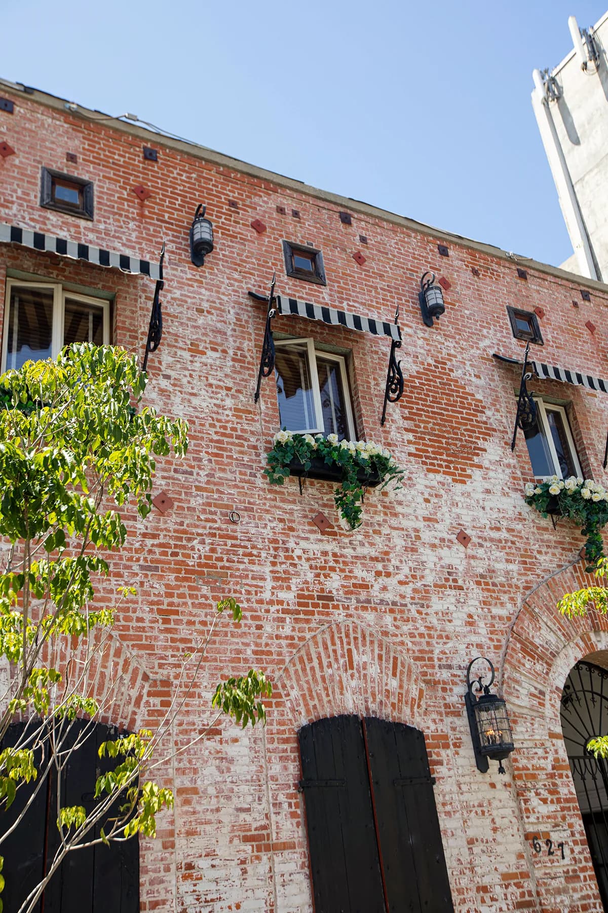 Historic brick building exterior with arched doorways, flower baskets and iron lanterns