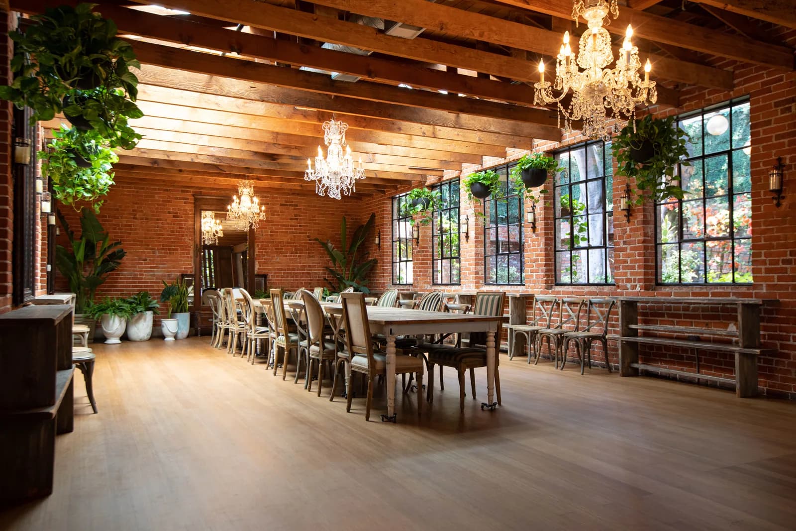 Elegant brick venue interior with chandeliers, wooden beams, dining tables and gridded windows overlooking a courtyard.