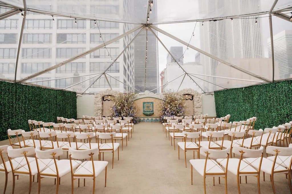 Wedding ceremony setup in elegant tent venue with green walls, wooden chairs, and floral altar