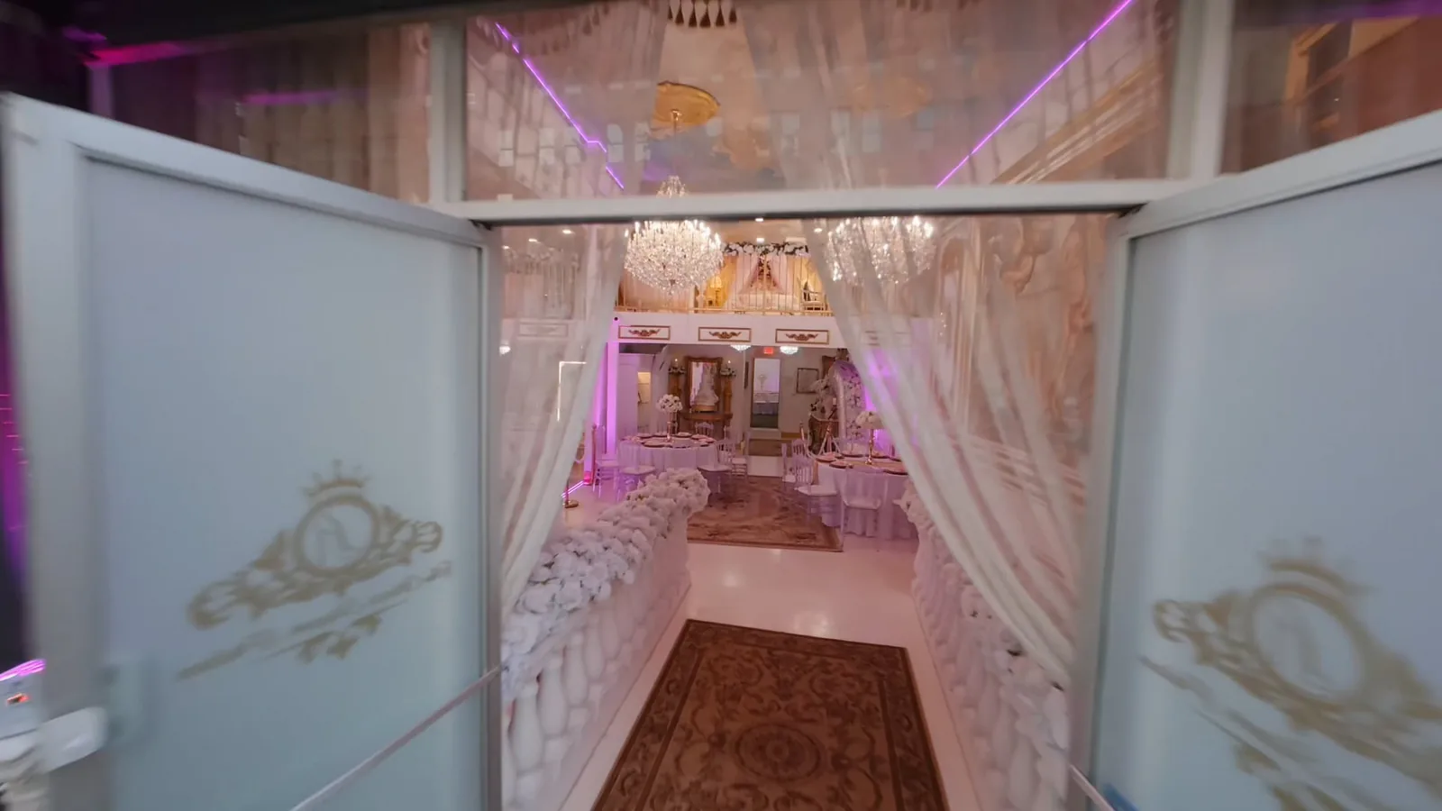 Elegant wedding venue entrance with purple-lit corridor, frosted glass doors, white drapes, and crystal chandelier