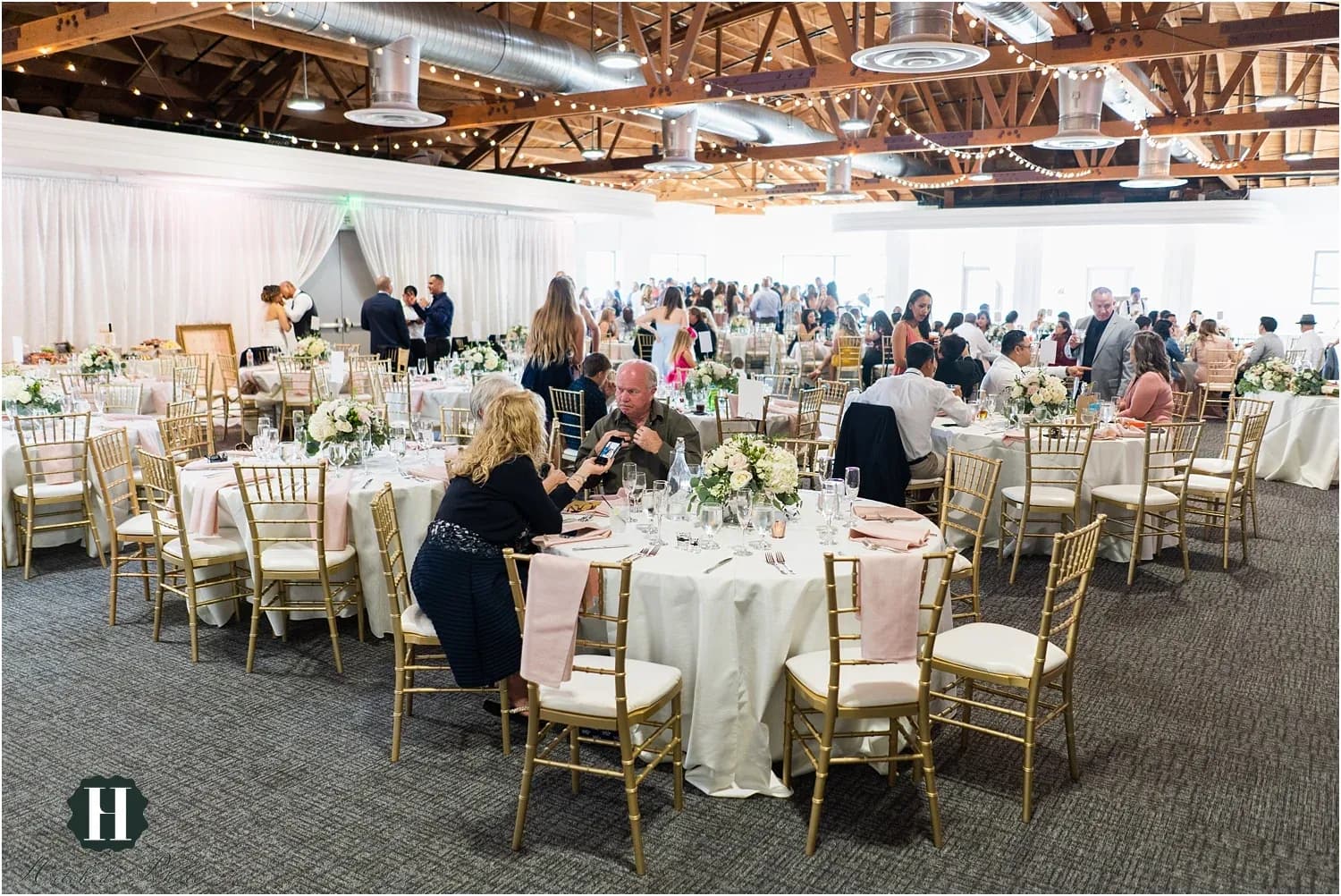 Wedding reception hall with round tables, gold chairs, white linens, and flower arrangements