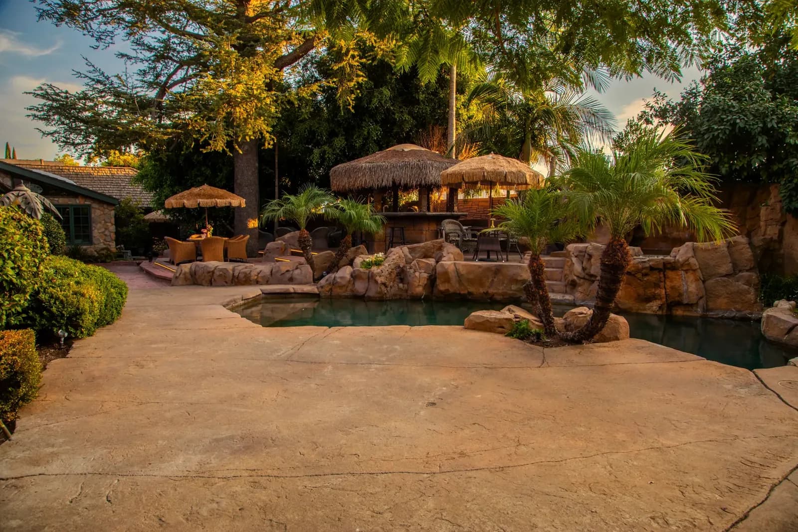 Tropical outdoor wedding venue with pool, tiki umbrellas, palm trees, and stone sitting areas