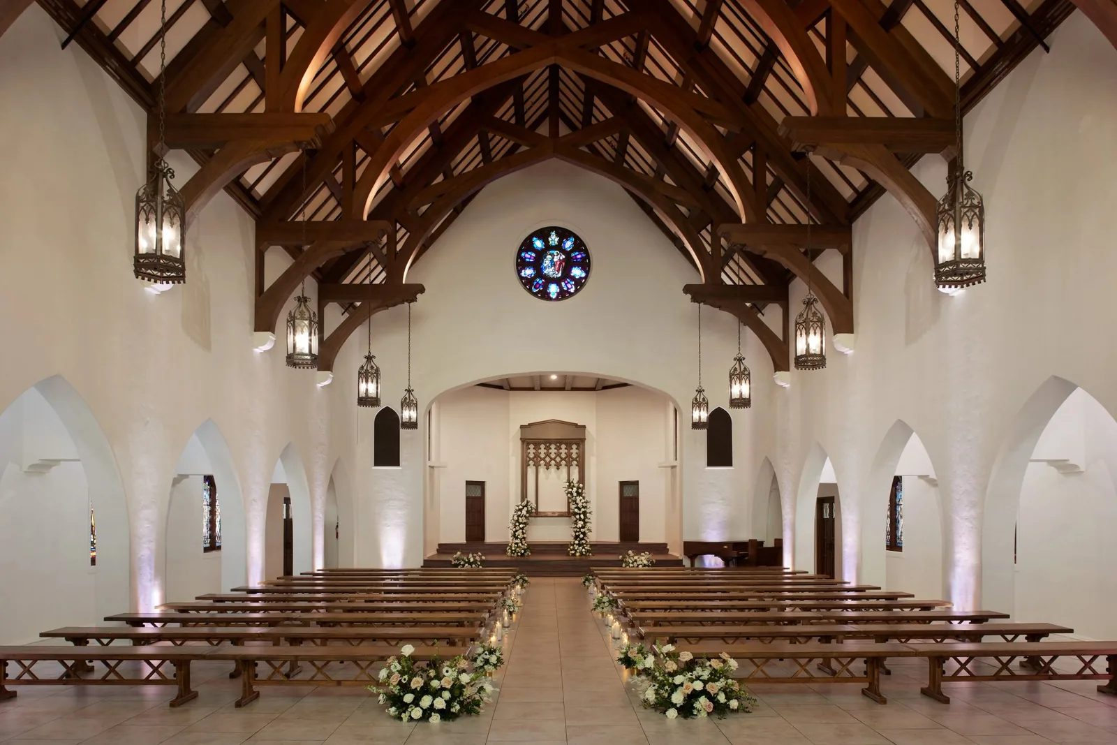 Chapel interior with wooden beams, stained glass, hanging lanterns, and flower-lined aisle